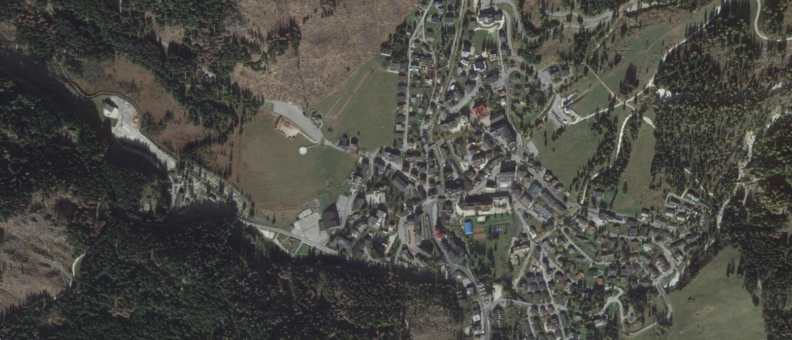 Vista aerea di un villaggio montano circondato da foreste e campi aperti.