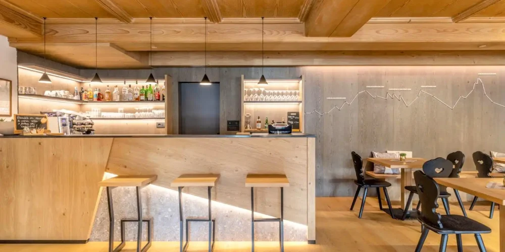 Interno di un bar moderno con arredi in legno e sgabelli al bancone.