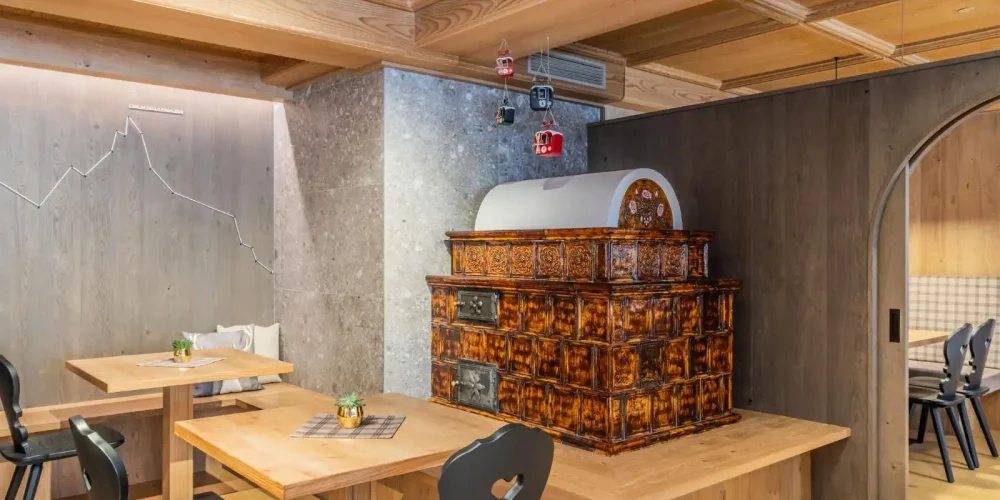 Interno di un ristorante con arredo in legno chiaro e stufa in maiolica decorata.