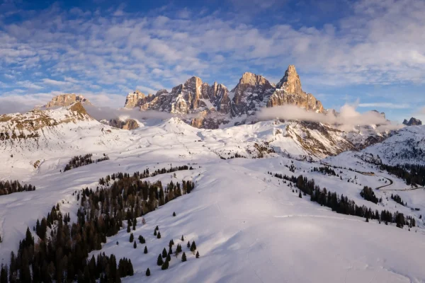 Paesaggio montano innevato con vista sulle Dolomiti sotto un cielo blu con nuvole sparse.